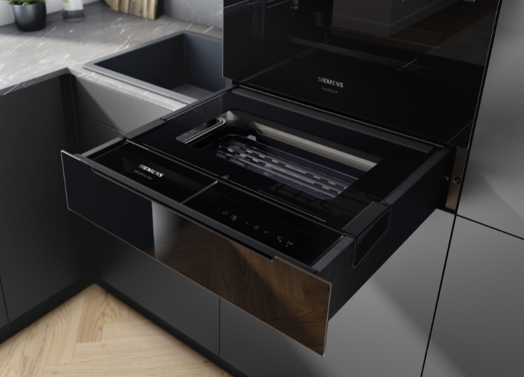 Geöffnete schwarze Dampfschublade unter einem Einbaubackofen mit sichtbarem Garbehälter und ausgezogenen Führungsschienen.