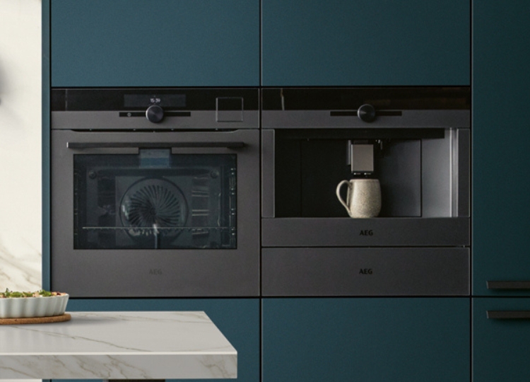 Schwarzer Einbaukaffeevollautomat neben einem Einbaubackofen in einer modernen Küche mit petrolfarbenen Schrankfronten.