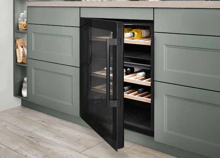 Geöffneter schwarzer Einbau-Weinkühlschrank mit Glasfront und Weinflaschen auf mehreren Ablagen in einer Küche mit grünen Kassettenfronten.