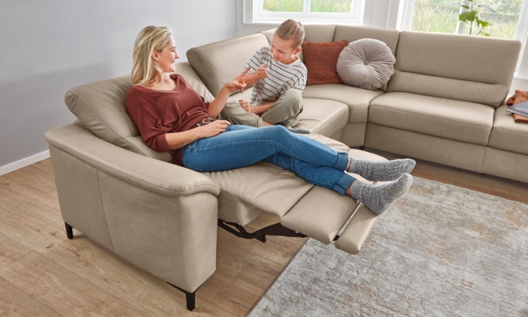 Frau und Kind entspannen auf einem beigefarbenen Sofa mit ausgefahrener Fußstütze und verstellbarer Rückenlehne.