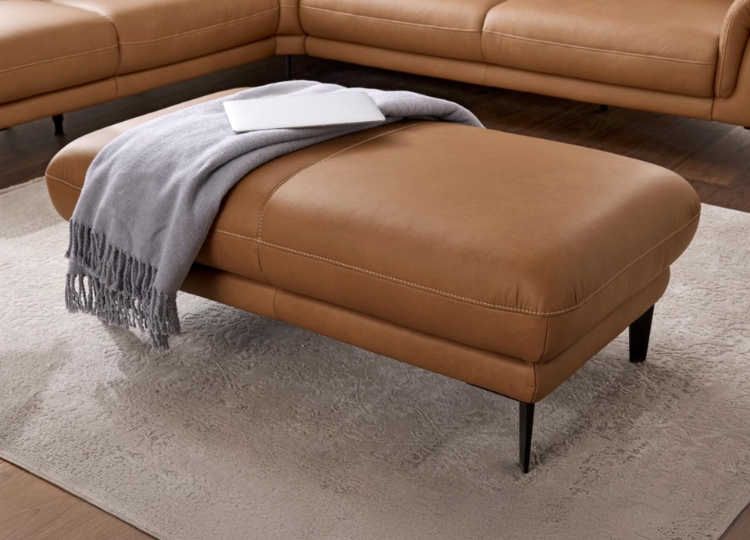 Cognacfarbener Lederhocker mit schwarzen Metallfüßen und grauer Decke vor einem passenden Ledersofa.