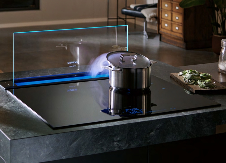 Siemens glassdraftAir Tischlüfter mit ausgefahrener transparenter Glasscheibe hinter einem Kochfeld in einer dunklen Küche.